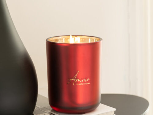 Rode Geurkaars Amour in glas, brandend op tafel, met warme gouden binnenkant en compact design