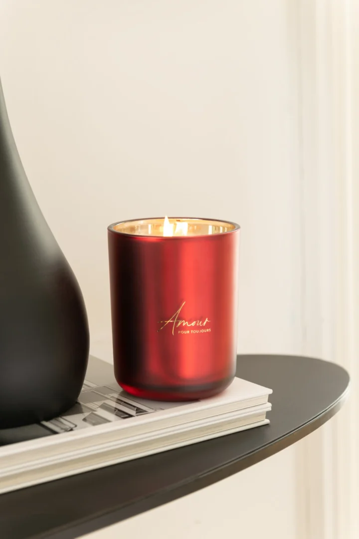 Rode Geurkaars Amour in glas, brandend op tafel, met warme gouden binnenkant en compact design