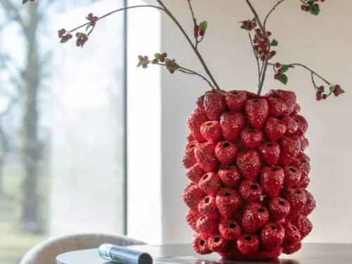Vaas Ceeldon van rode klei met glazuur, gevuld met takken, op tafel in warm interieur