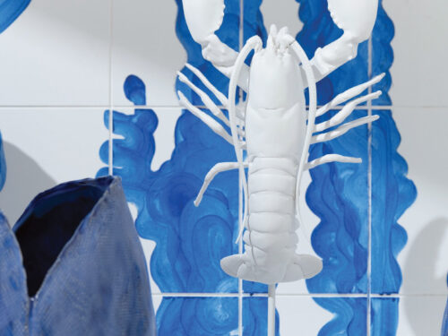 Witte kreeftvormige vaas op standaard voor blauw getegelde wand, met organische armen en scharen