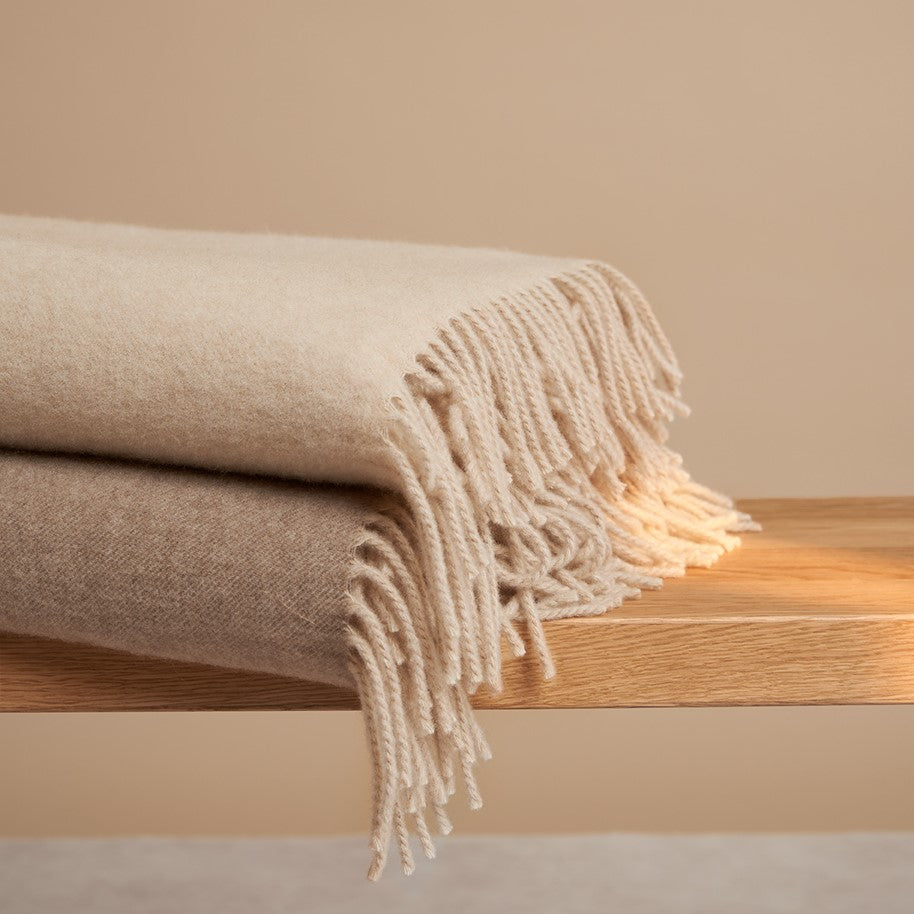 Plaid Daulloro cashmere plaid in subtiele beige tinten met zachte franjes op een houten bankje