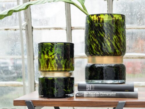 Groene glazen Vaas Trudir met messing detail op houten tafel, gevuld met blad, in elegant interieur