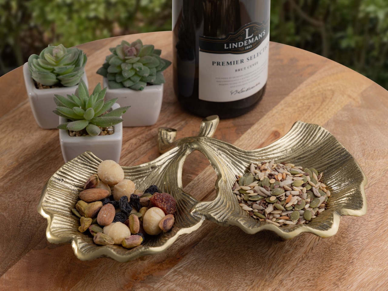 Schaal Fleevund aluminium zilver in Ginkgo-vorm, gevuld met noten en zaden op houten tafel