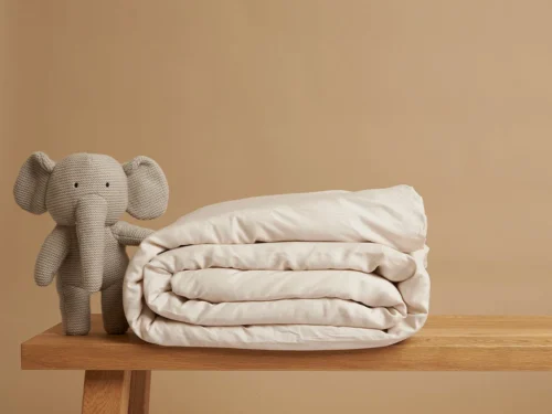 Dekbedovertrek Jeery Beige met zachte Tencel, opgevouwen naast knuffelelefant op houten tafel