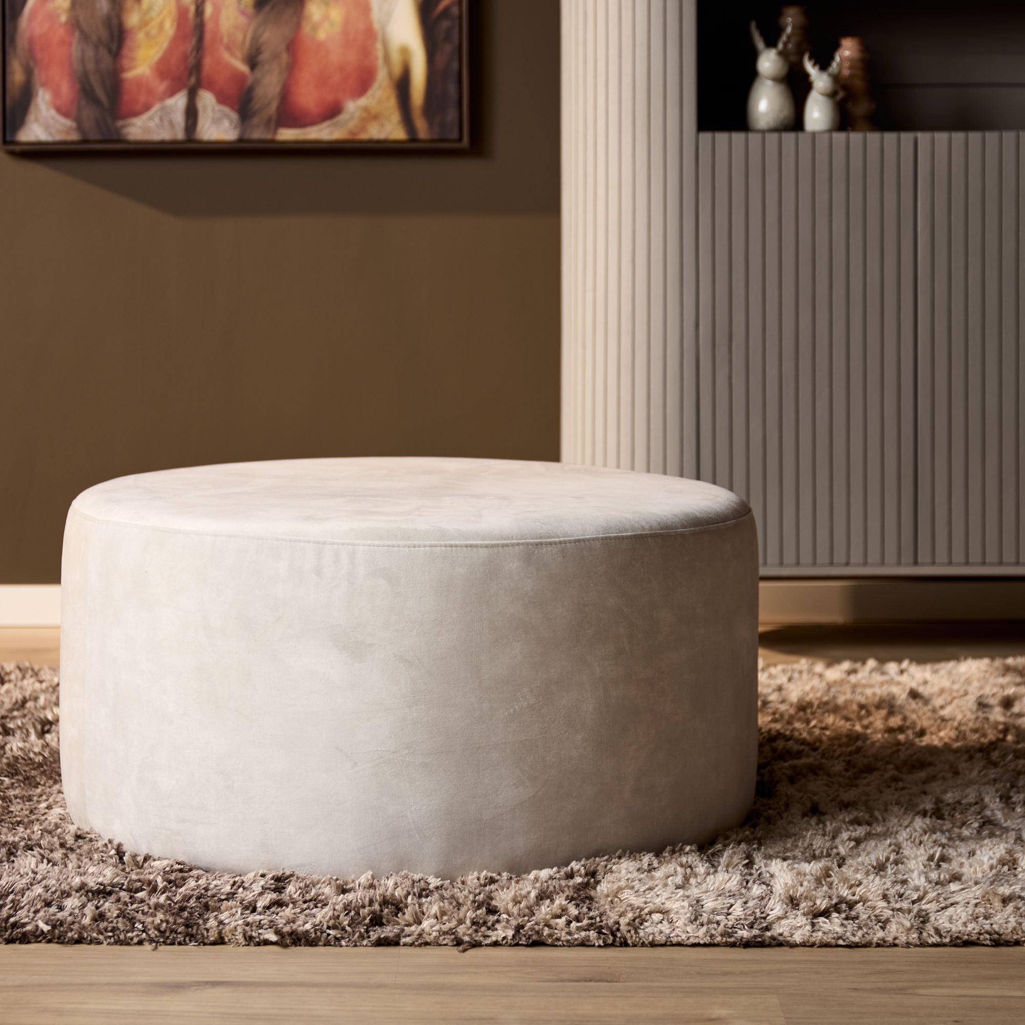 Poef Seevo Crème, ronde hocker in zachte Adore 102 bekleding op een hoogpolig vloerkleed