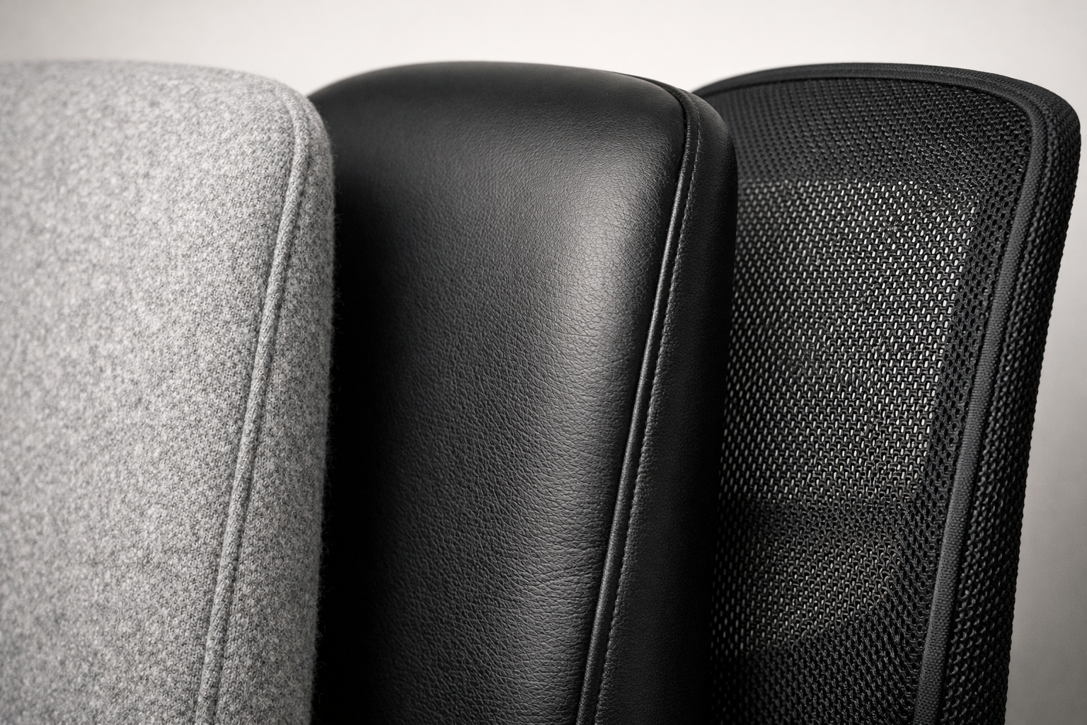 Rugleuningen van bureaustoelen naast elkaar in grijze wol, zwart leer en zwarte mesh