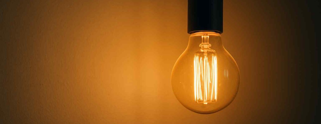 Gloeilamp met warm licht tegen een bruine achtergrond. De lamp is helder en de achtergrond is donkerder. Design element voor een zitbank.