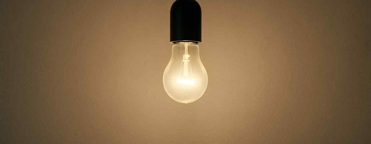 Een gloeilamp met zwart snoer en fitting tegen een beige achtergrond. Warm licht schijnt op de muur. Design voor jouw woonkamer.