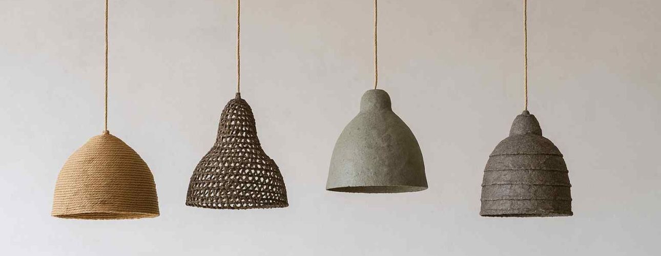 Vier hanglampen van gerecyclede materialen tegen een witte achtergrond. De lampen hebben verschillende vormen en texturen in bruin en grijs.