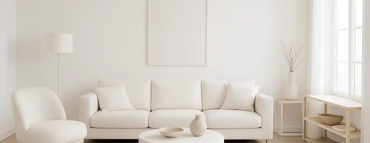 Minimalistische woonkamer met een witte bank, ronde salontafel, accentstoel en staande lamp. Waarom wit interieur? Neutrale tinten en natuurlijk licht creëren een lichte, luchtige sfeer, terwijl decoratieve vazen en gedroogde takken de ruimte accentueren.