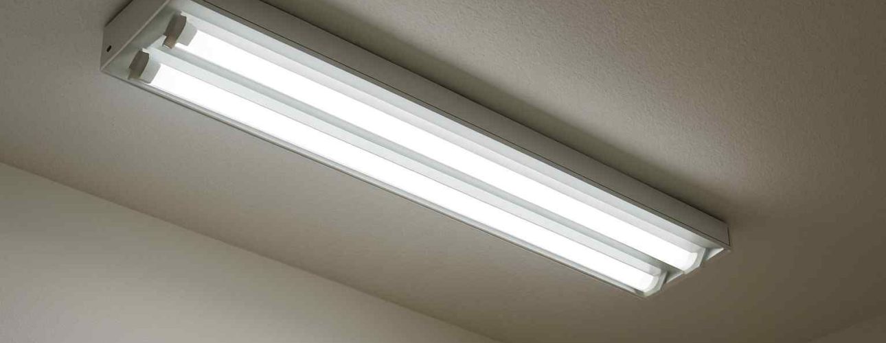 Witte TL-balk aan een plafond, gezien vanuit een lage hoek. De lamp heeft vier buizen en een metalen frame. Neutrale kleuren in de achtergrond.