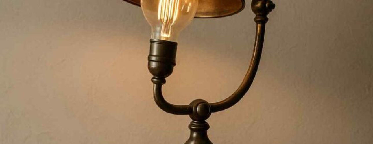 Vintage lamp met gloeilamp op houten kastje. De lamp heeft een bronzen kleur en een gebogen arm. Sfeervolle verlichting voor de woonkamer.